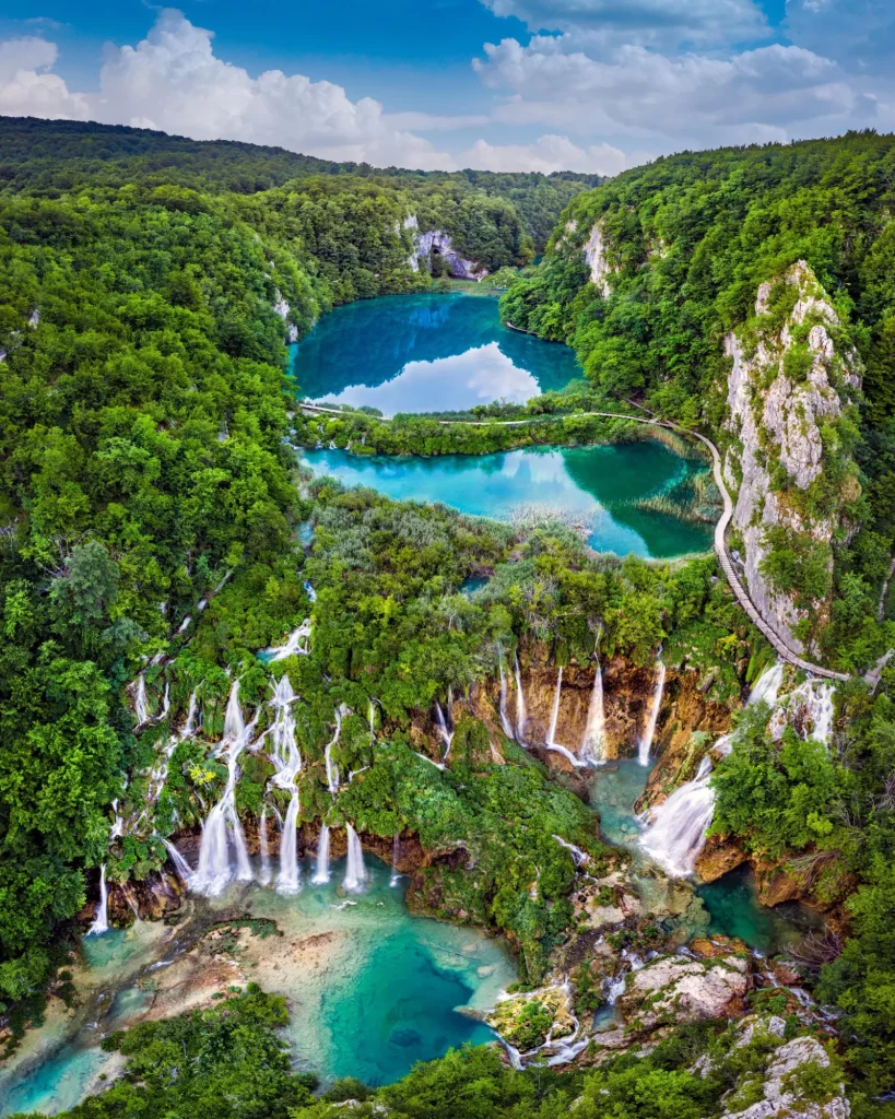 Plitvice, Kroatien - Fantastisk utsikt över de vackra vattenfallen vid Plitvicesjöarna i Plitvices nationalpark på en ljus sommardag med blå himmel och moln och grönt lövverk och turkost vatten